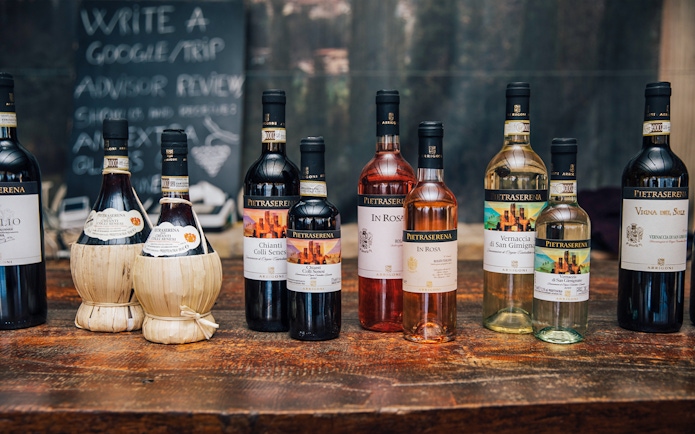 Bottles of Tuscan wine on a wooden table, featuring Chianti and Vernaccia di San Gimignano.