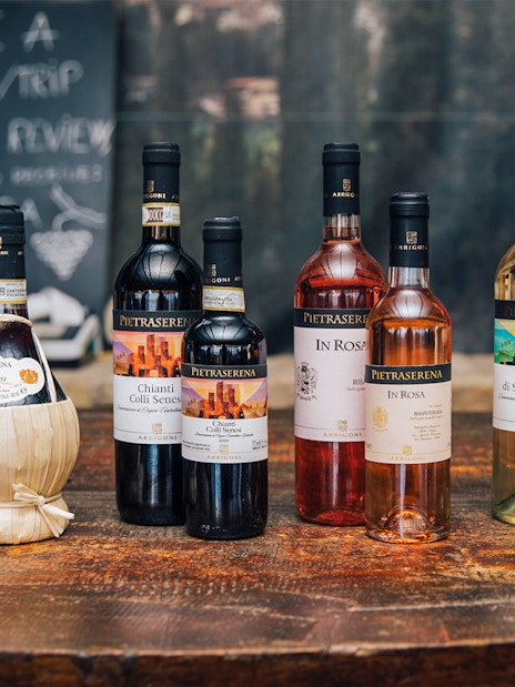 Bottles of Tuscan wine on a wooden table, featuring Chianti and Vernaccia di San Gimignano.