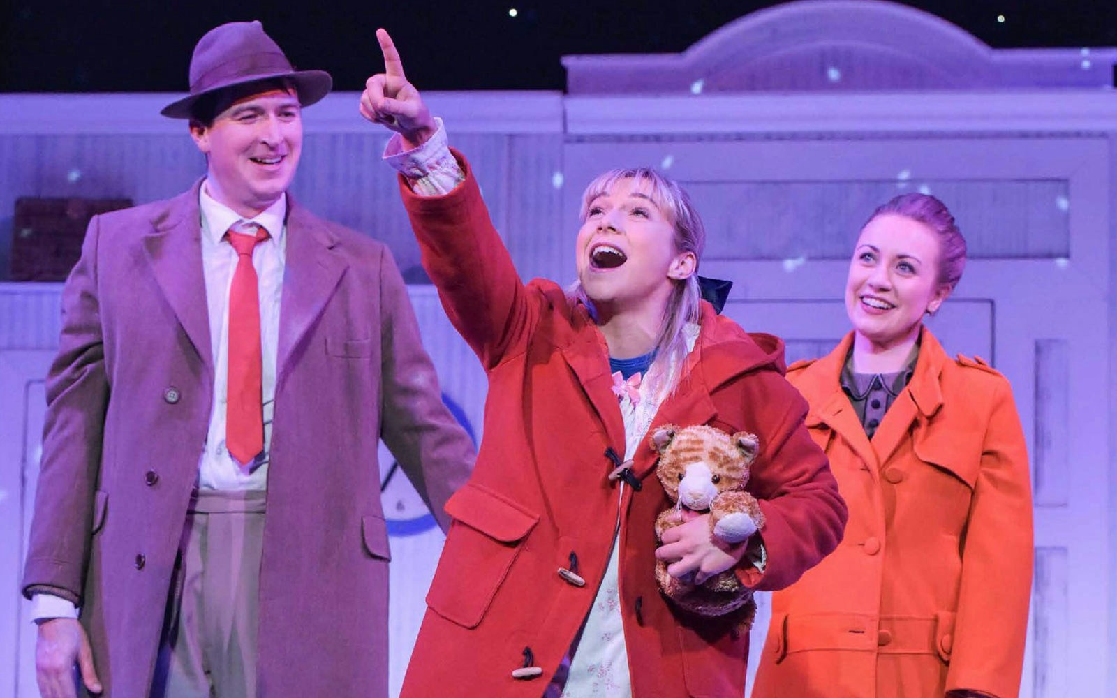 Child holding a stuffed tiger, pointing excitedly, with two adults smiling in a theater setting.
