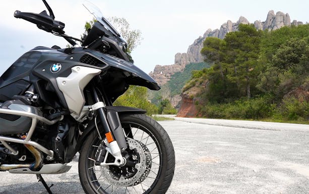 BMW R1250GS motorcycle on road with Montserrat mountains in Barcelona background.