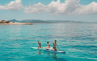 Tourists paddleboarding on clear waters during Ibiza to Formentera cruise.
