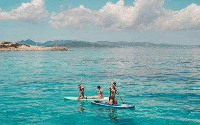 Tourists paddleboarding on clear waters during Ibiza to Formentera cruise.