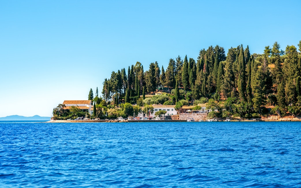 Kouloura Bay view from the sea, Corfu, Greece, with lush greenery and coastal buildings.