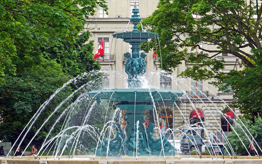 Fountain in front of a historic building with Swiss flags in Geneva.