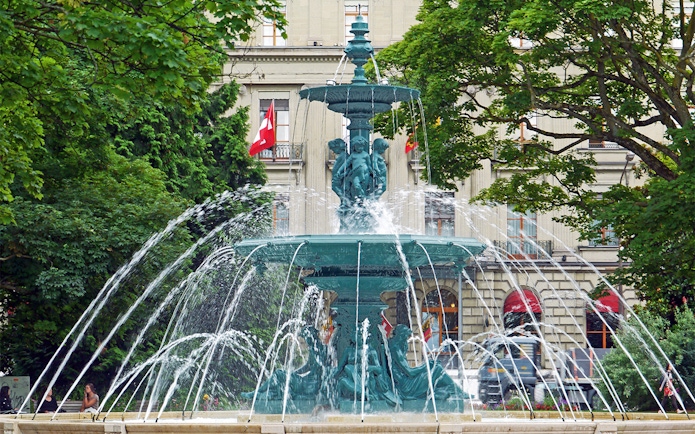 Fountain in front of a historic building with Swiss flags in Geneva.