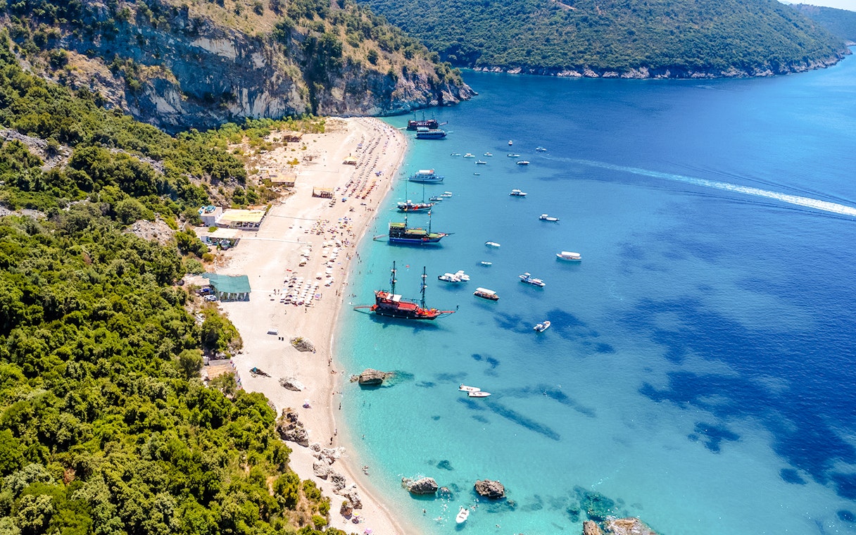 Aerial view of Kroreza Beach, Albania with boats along the shoreline and lush green hills.