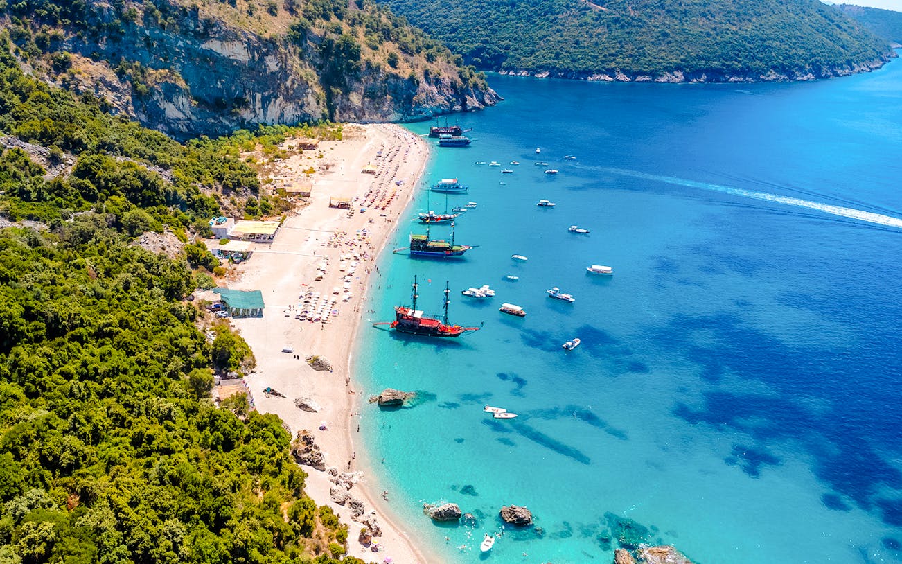 Aerial view of Kroreza Beach, Albania with boats along the shoreline and lush green hills.