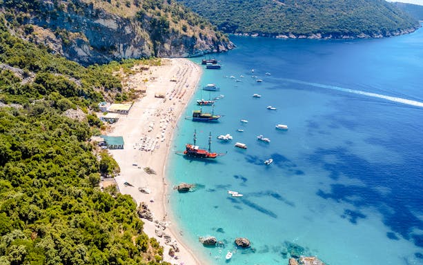 Aerial view of Kroreza Beach, Albania with boats along the shoreline and lush green hills.
