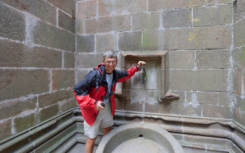 Visitor at Mont Saint-Michel fountain during Paris day trip.