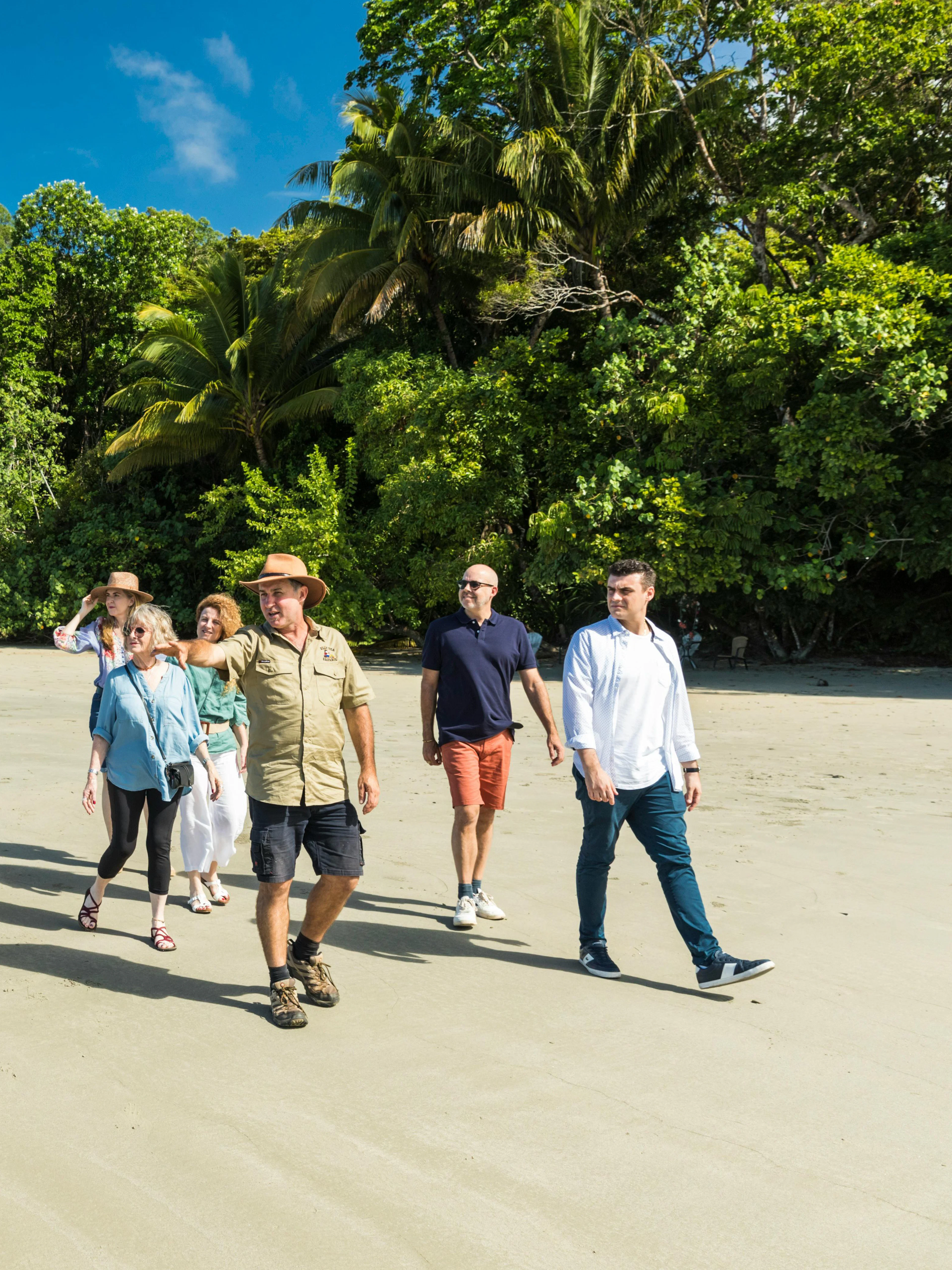 Group walking on a sandy beach in Daintree Rainforest, surrounded by lush greenery, during a guided tour.