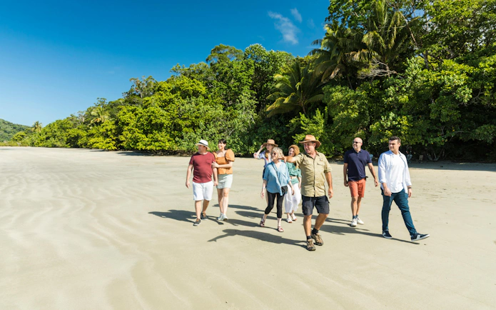 Group walking on a sandy beach in Daintree Rainforest, surrounded by lush greenery, during a guided tour.