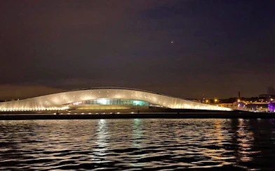 MAAT museum in Lisbon illuminated at night, reflecting on the Tagus River.