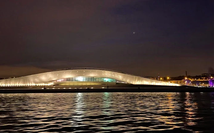 MAAT museum in Lisbon illuminated at night, reflecting on the Tagus River.
