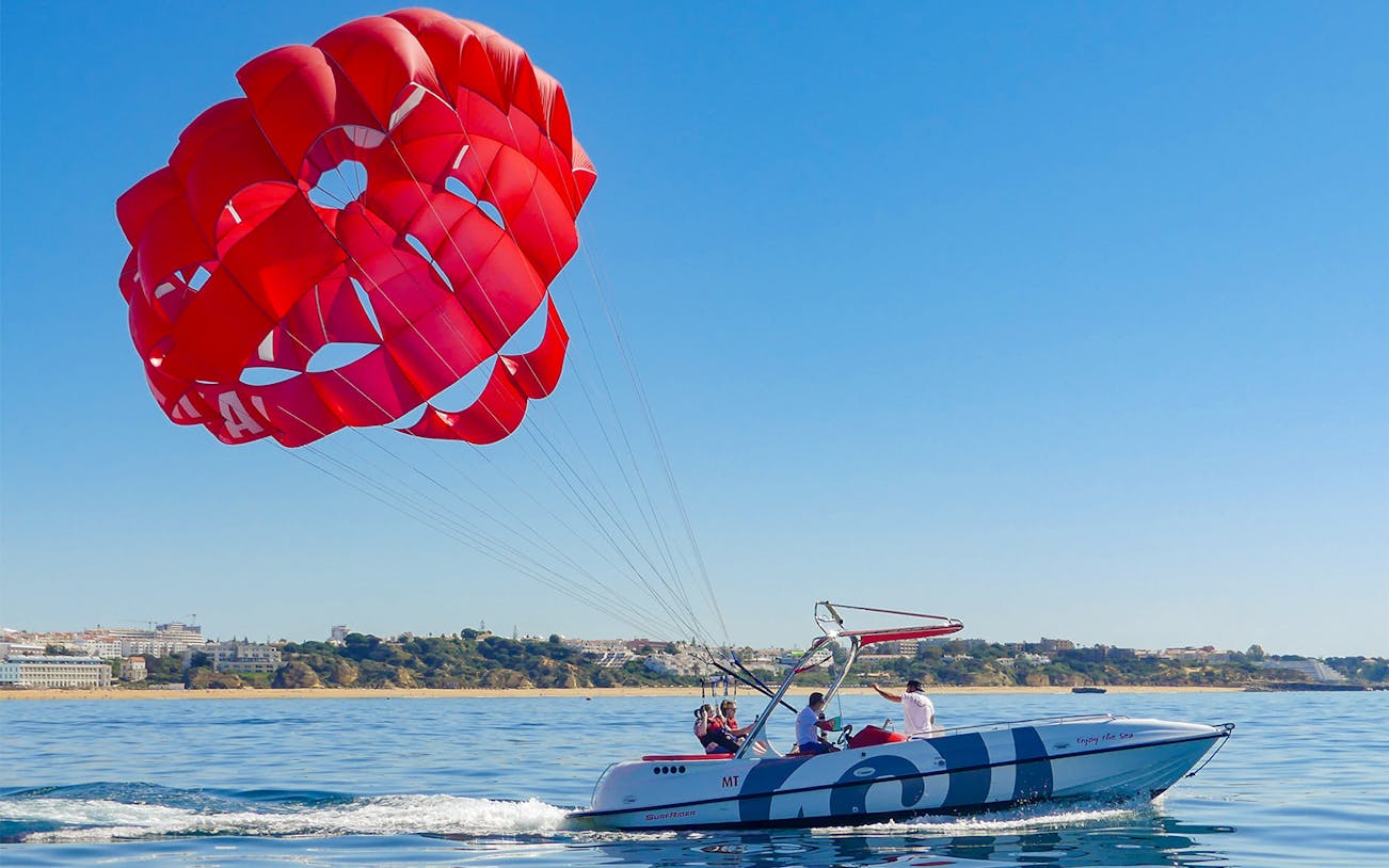 Parasailing over the ocean in Albufeira with a red parachute and speedboat.