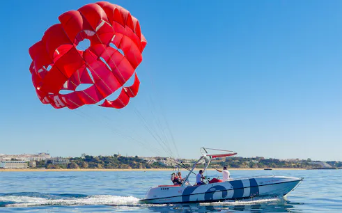 Parasailing over the ocean in Albufeira with a red parachute and speedboat.