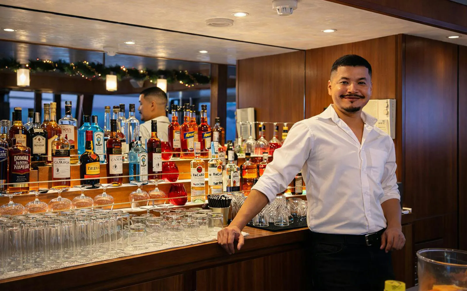 Bartender at open bar on Lisbon sunset boat party cruise with various liquor bottles.