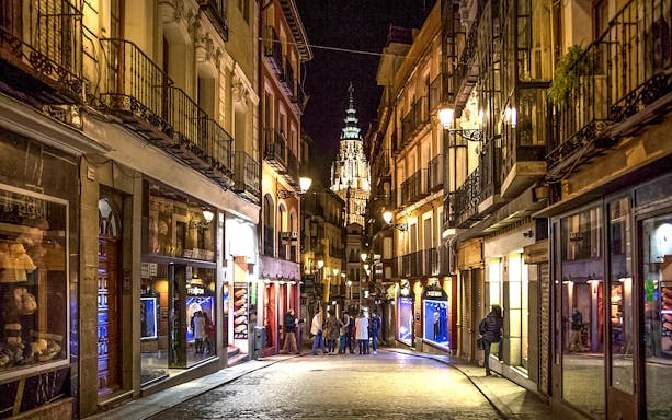 Street in Toledo at night with illuminated cathedral in the background, capturing "Una Mágica noche Toledana.