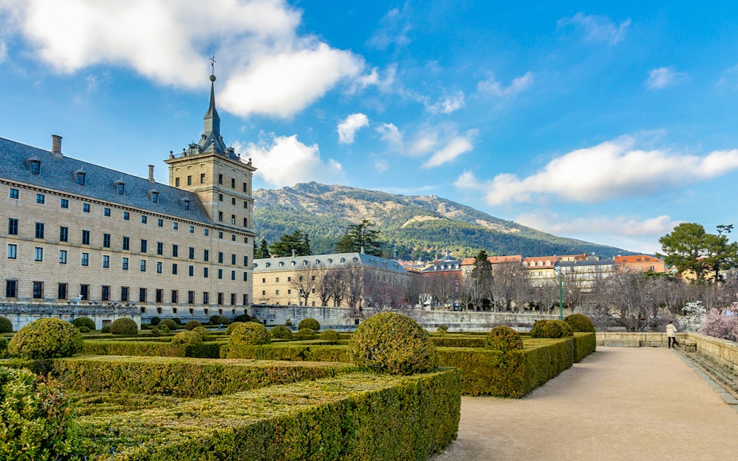 Royal Site of San Lorenzo de El Escorial with gardens and mountain backdrop.