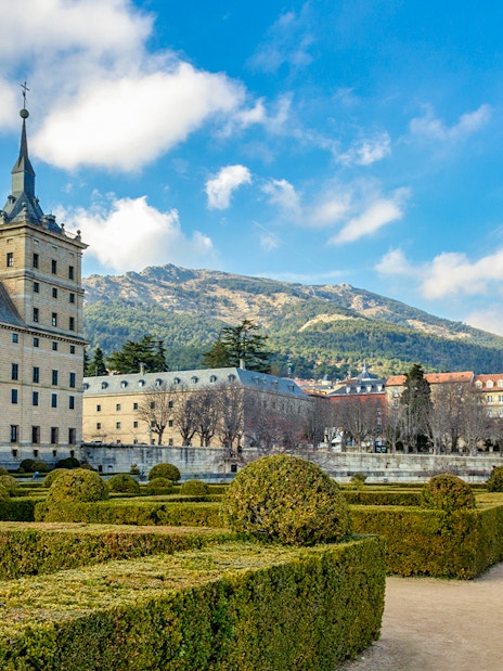 Royal Site of San Lorenzo de El Escorial with gardens and mountain backdrop.