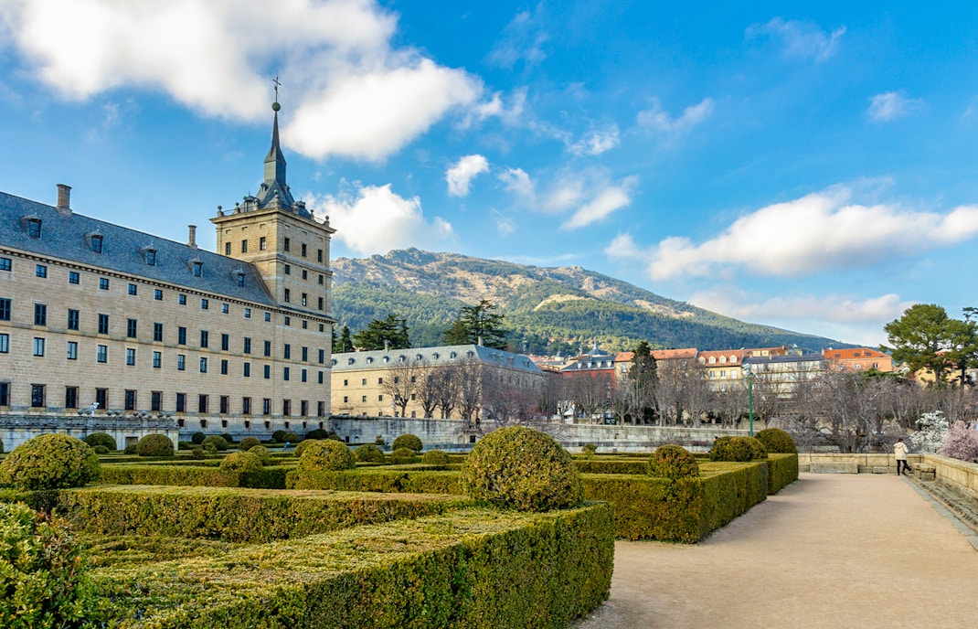 Royal Site of San Lorenzo de El Escorial with gardens and mountain backdrop.