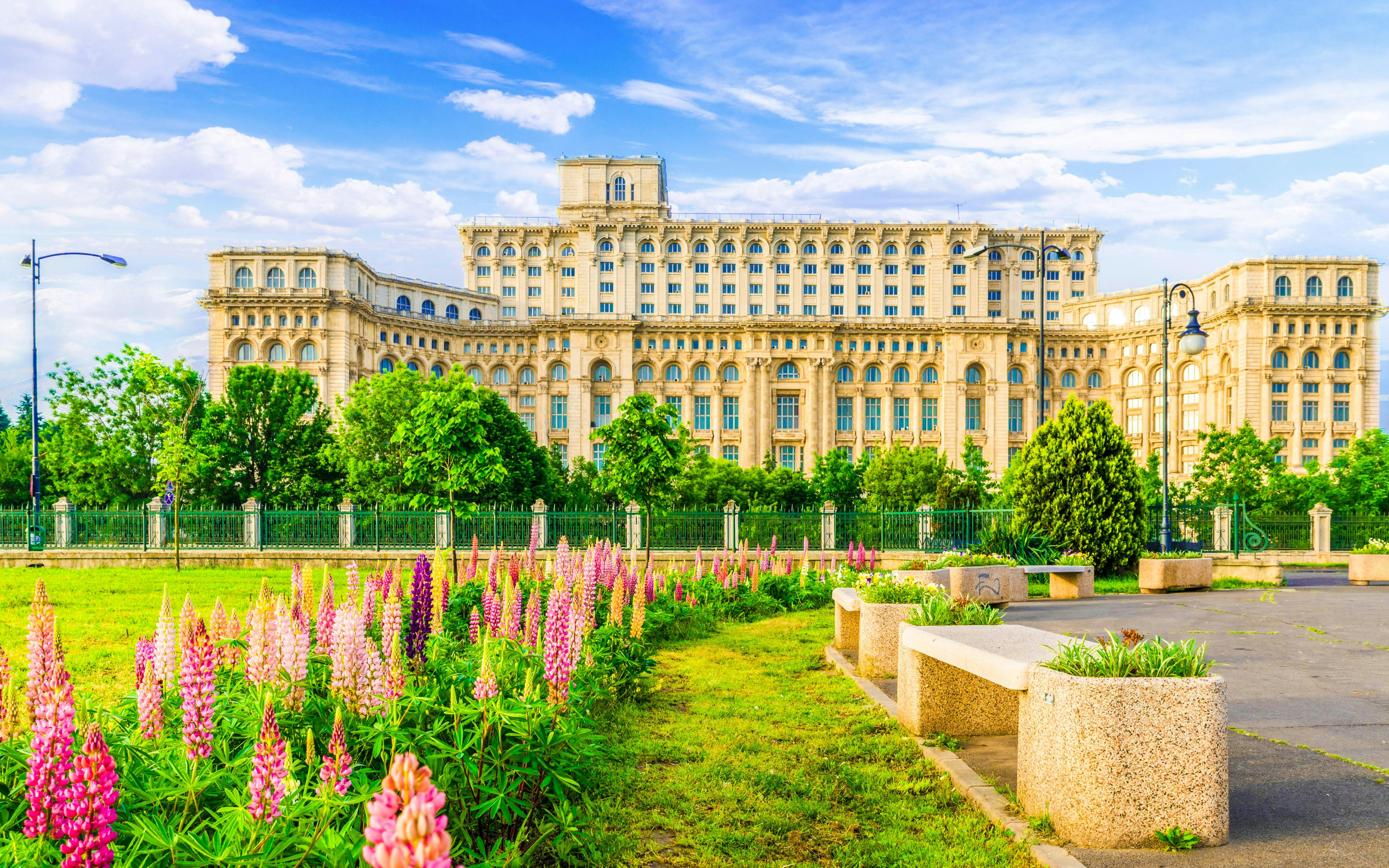 Palace of Parliament in Bucharest with gardens and colorful flowers in foreground.