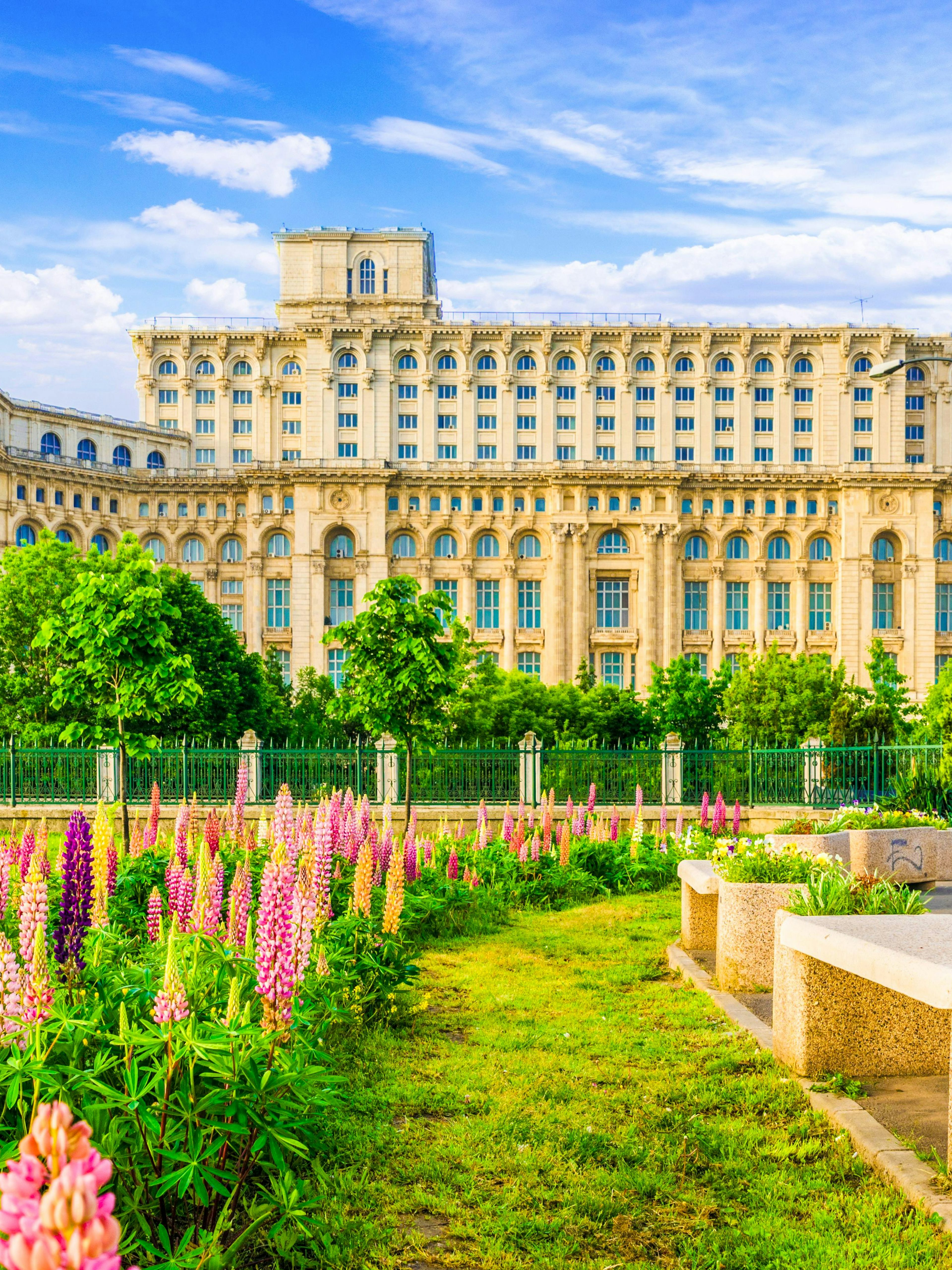 Palace of Parliament in Bucharest with gardens and colorful flowers in foreground.
