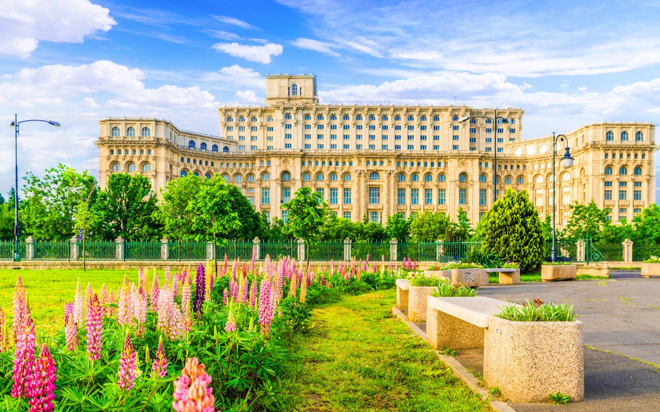 Palace of Parliament in Bucharest with gardens and colorful flowers in foreground.