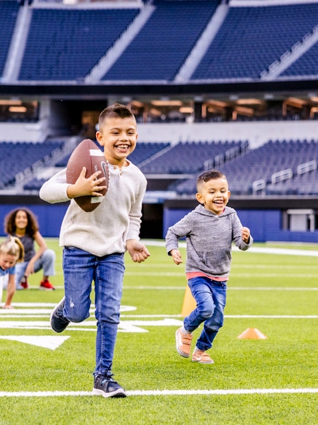 Children playing football on a field in Los Angeles stadium, part of Go City Pass experience.