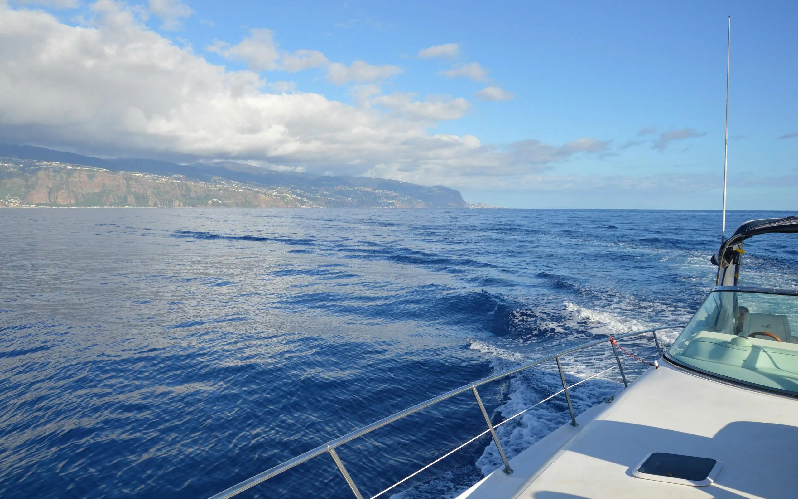 Boat on ocean near Calheta, Madeira, with distant coastline view.