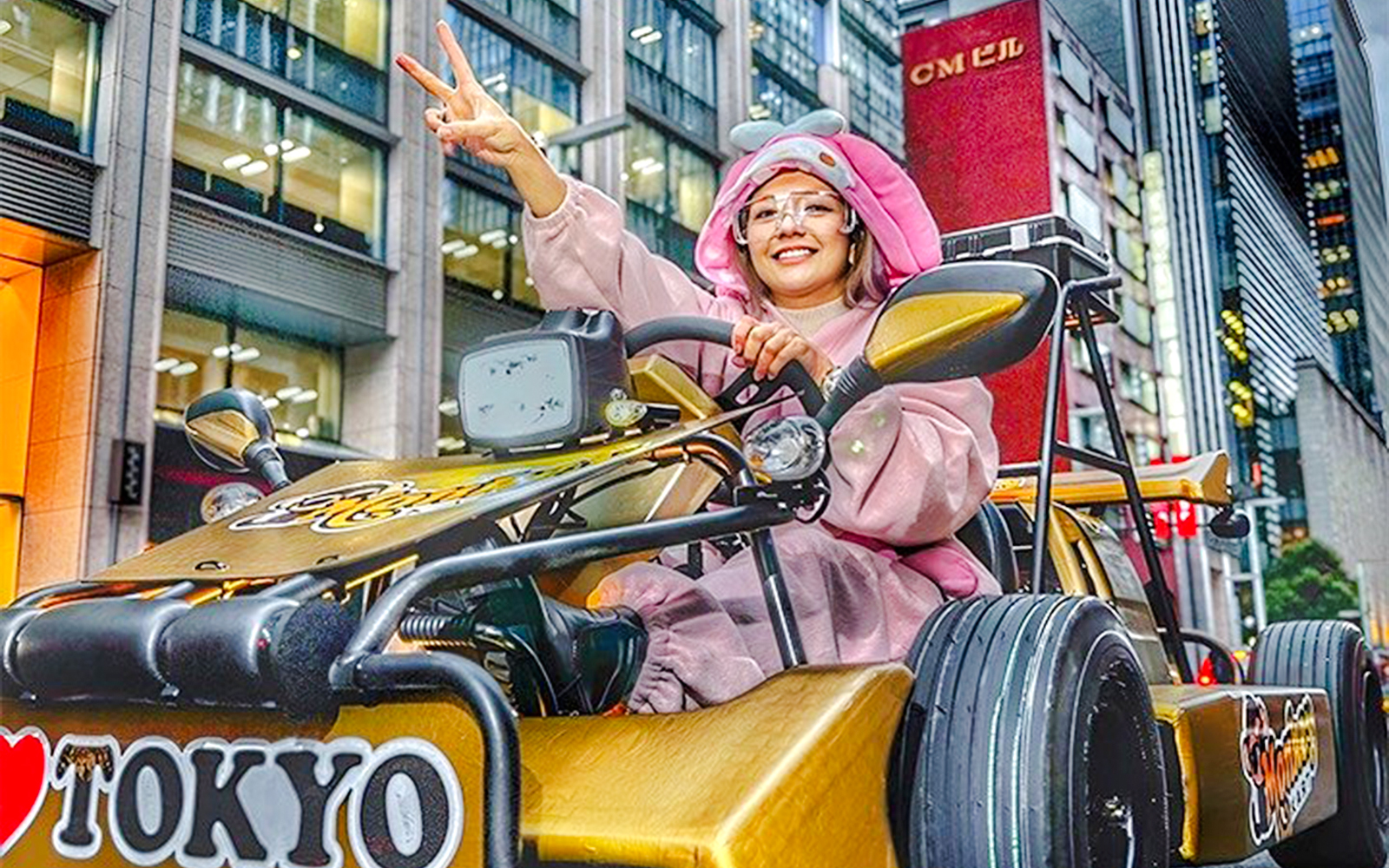 Woman in pink bunny costume driving a go-kart, giving peace sign in Tokyo.