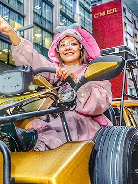 Woman in pink bunny costume driving a go-kart, giving peace sign in Tokyo.