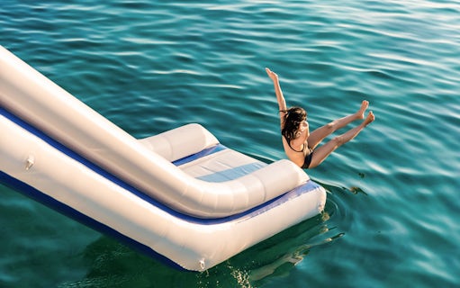 Person sliding into emerald green water from inflatable slide, surrounded by limestone mountains.