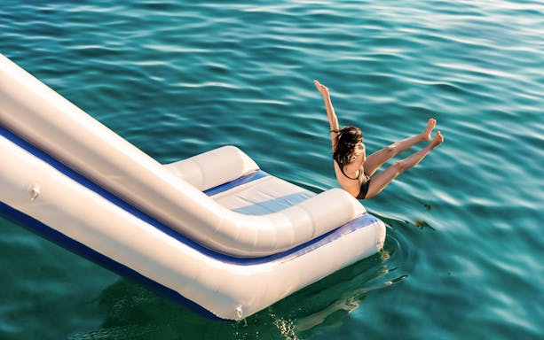 Person sliding into emerald green water from inflatable slide, surrounded by limestone mountains.