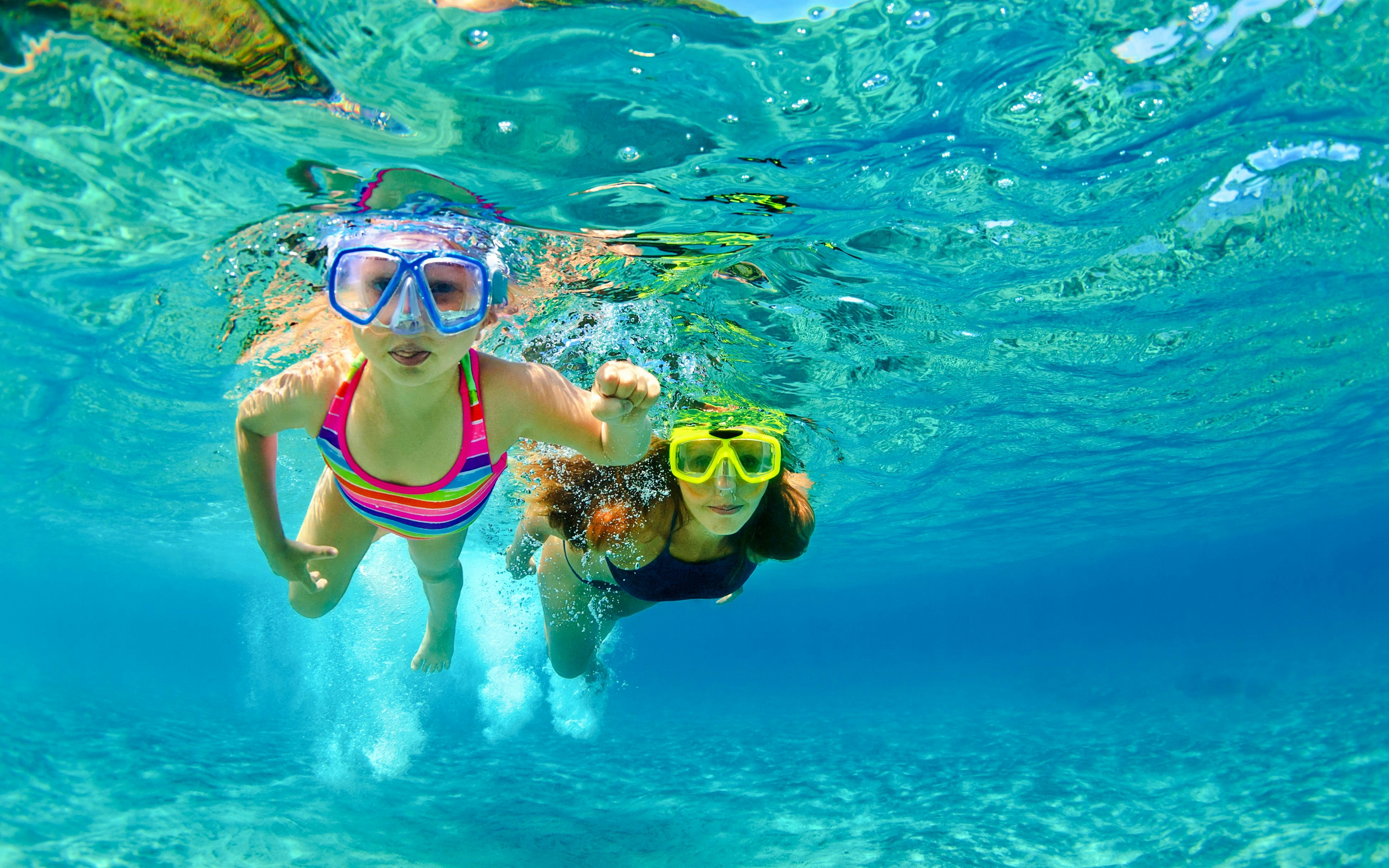 Mother and child snorkeling in clear blue water.