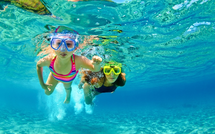 Mother and child snorkeling in clear blue water.