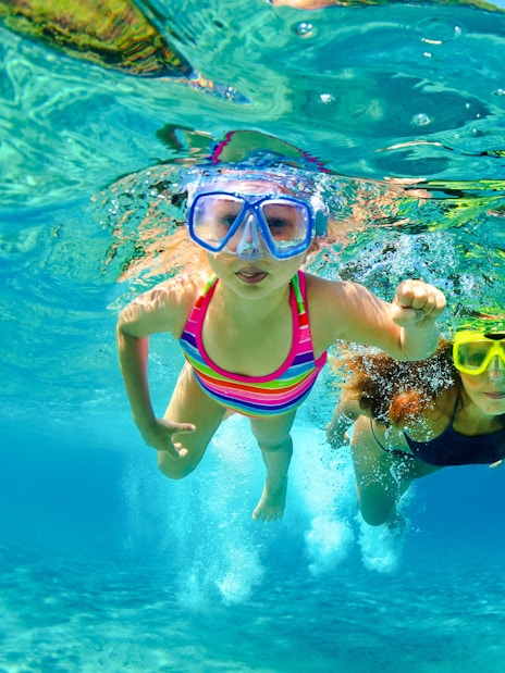 Mother and child snorkeling in clear blue water.