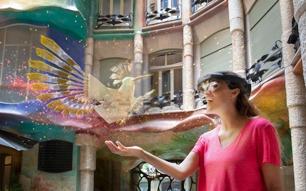 Woman experiencing La Pedrera Virtual Experience with holographic bird in courtyard.