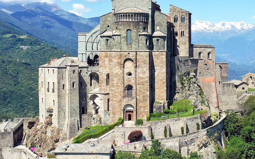 Sacra di San Michele monastery on a hilltop with mountains in the background, Italy.