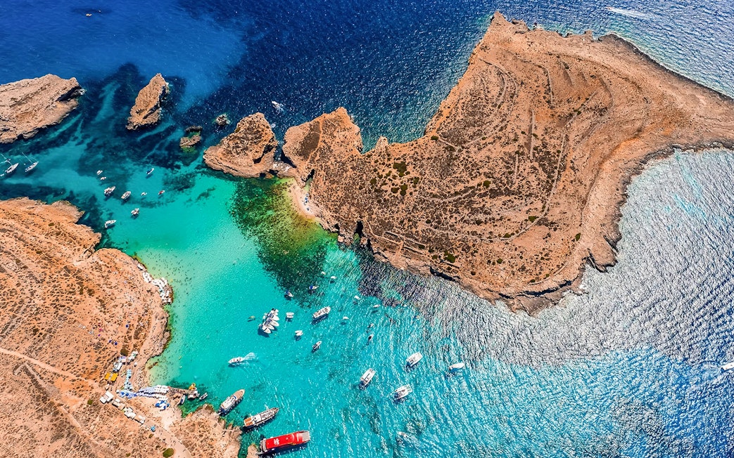 Aerial view of boats in the Blue Lagoon, Malta, surrounded by clear turquoise water and rocky coastline.