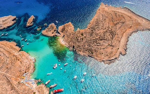 Aerial view of boats in the Blue Lagoon, Malta, surrounded by clear turquoise water and rocky coastline.