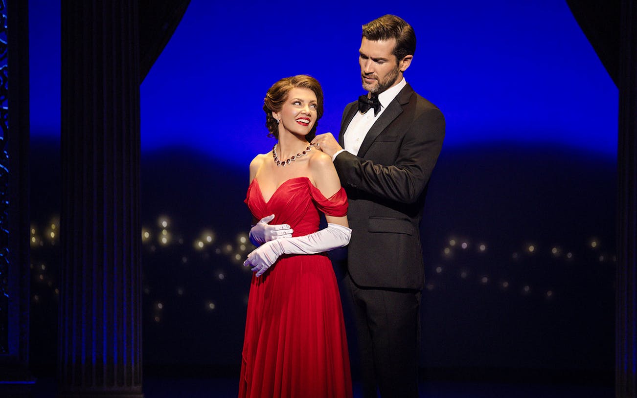 Cast in elegant attire during a scene from Pretty Woman The Musical with a vibrant backdrop.