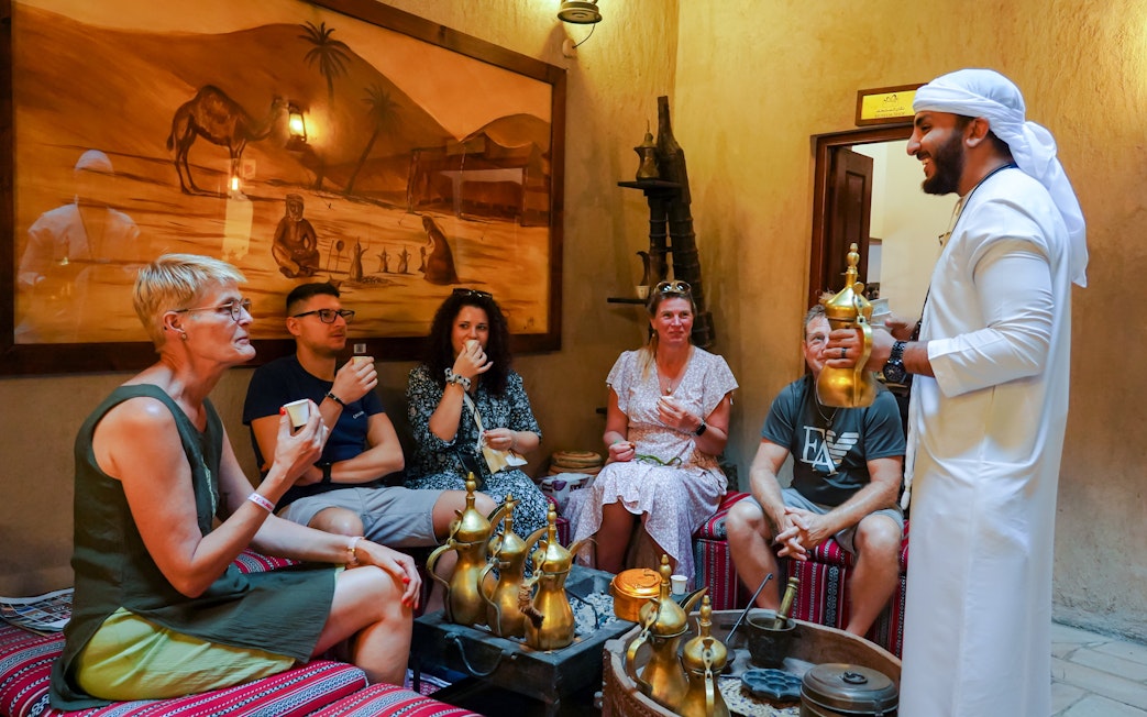 Visitors enjoying Arabic coffee in a traditional setting with a host in Dubai.