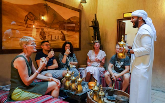Visitors enjoying Arabic coffee in a traditional setting with a host in Dubai.