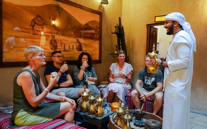 Visitors enjoying Arabic coffee in a traditional setting with a host in Dubai.