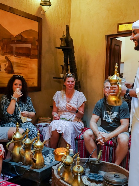 Visitors enjoying Arabic coffee in a traditional setting with a host in Dubai.