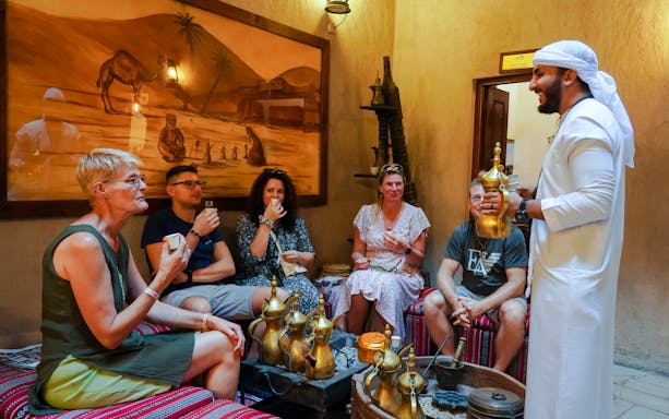 Visitors enjoying Arabic coffee in a traditional setting with a host in Dubai.