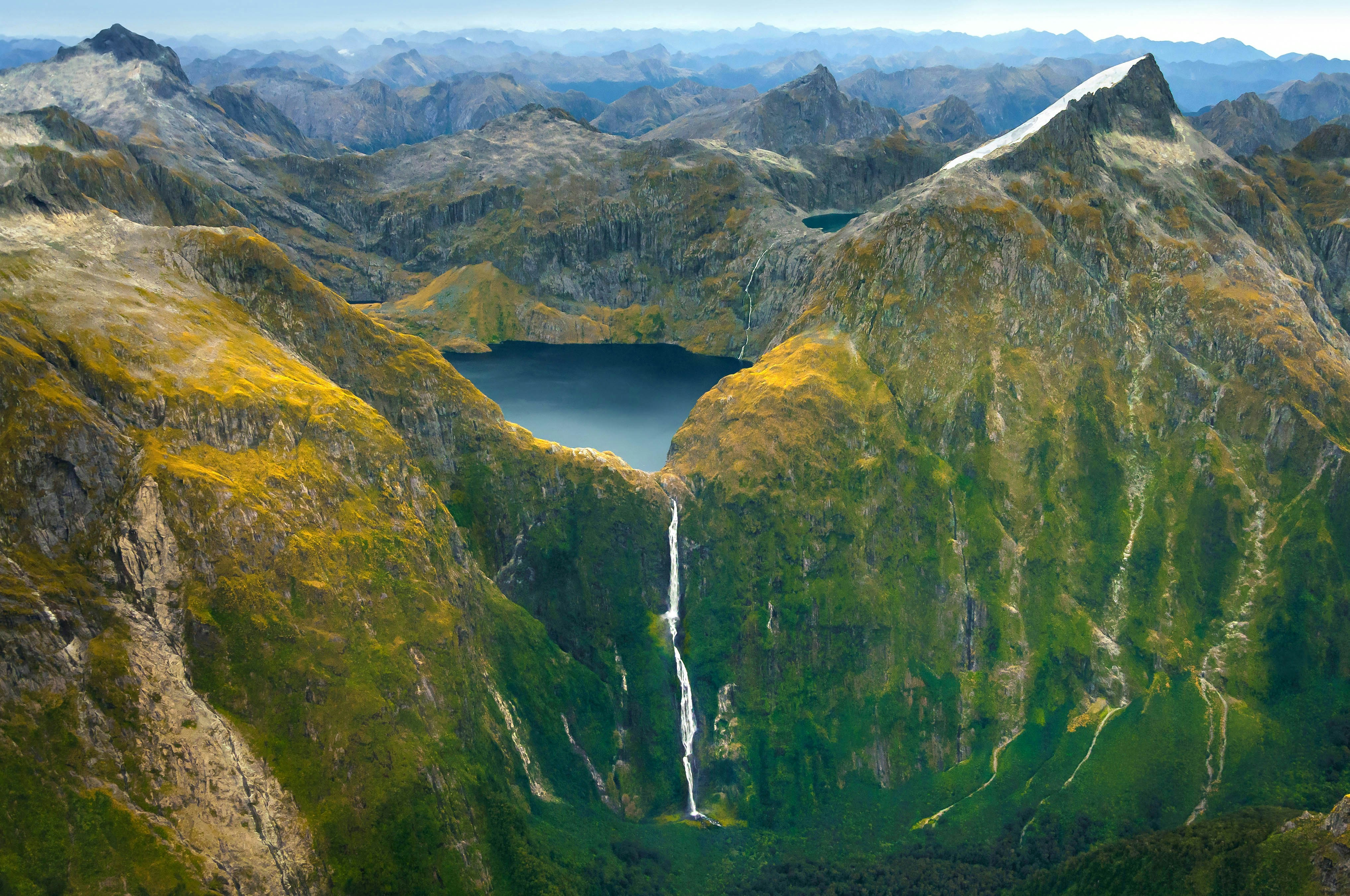 Aerial view of Sutherland Falls cascading down lush green mountains in Fiordland National Park, New Zealand.