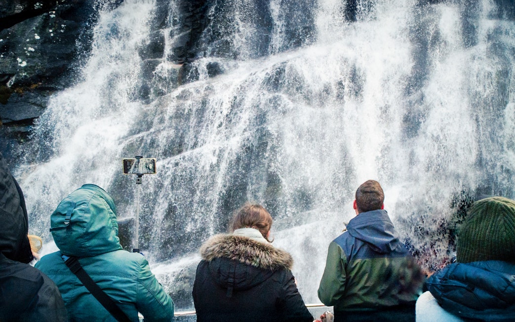Visitors photographing waterfalls on Mostraumen Fjord Cruise in Norway.