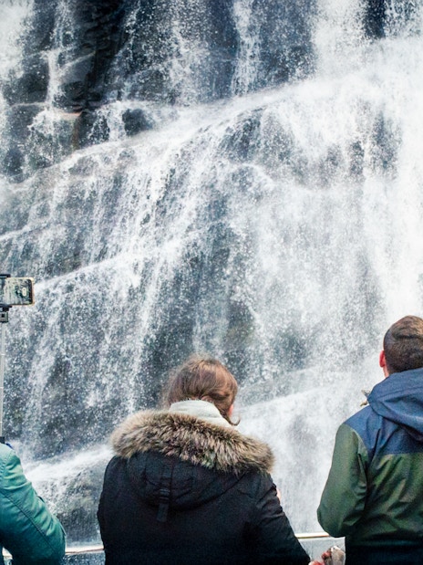 Visitors photographing waterfalls on Mostraumen Fjord Cruise in Norway.