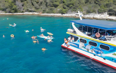 Tourists swimming near a cruise boat in Split, Croatia, with inflatable floats and nearby islands.